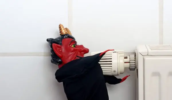 A red demon figurine dressed in black turning a radiator thermostat