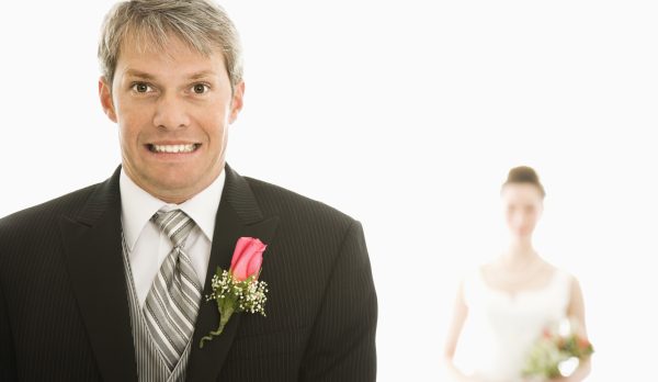 A groom looking nervous as his bride approaches from behind him