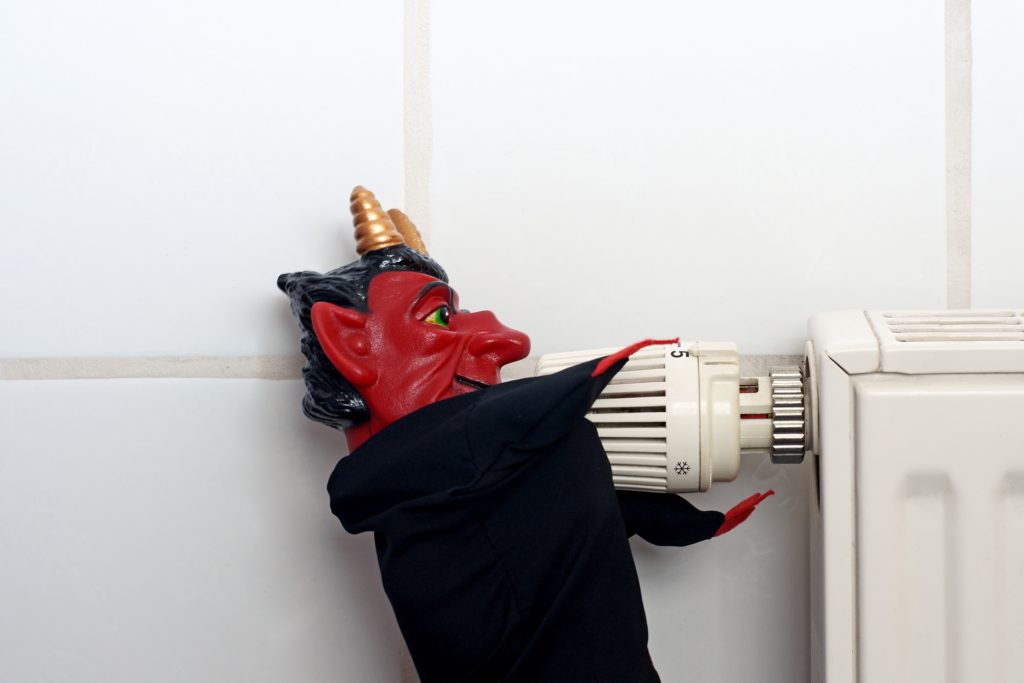 A red demon figurine dressed in black turning a radiator thermostat