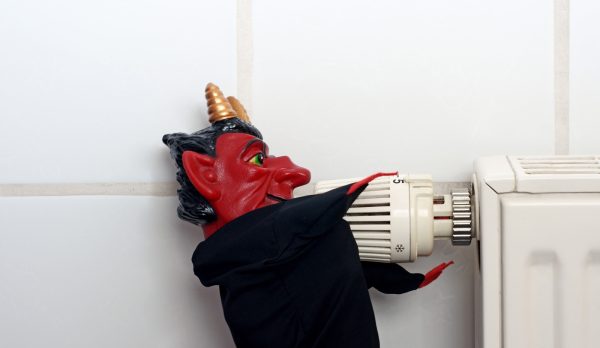 A red demon figurine dressed in black turning a radiator thermostat