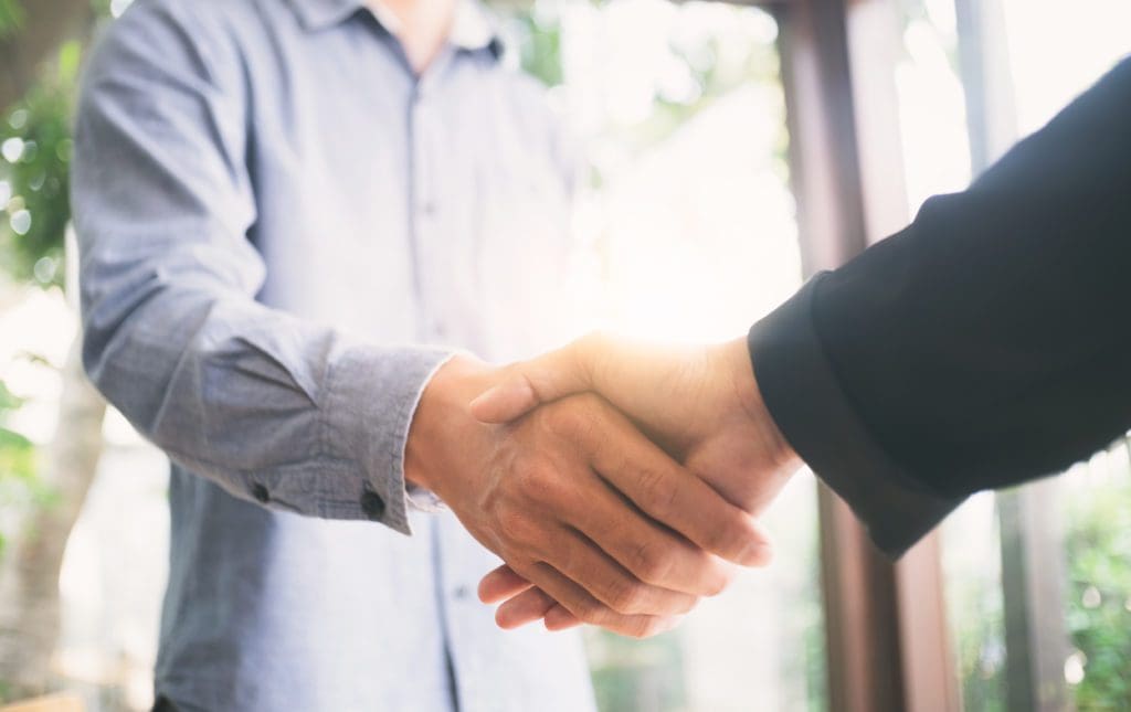 Two people shaking hands with an overexposed background that looks like light shining through