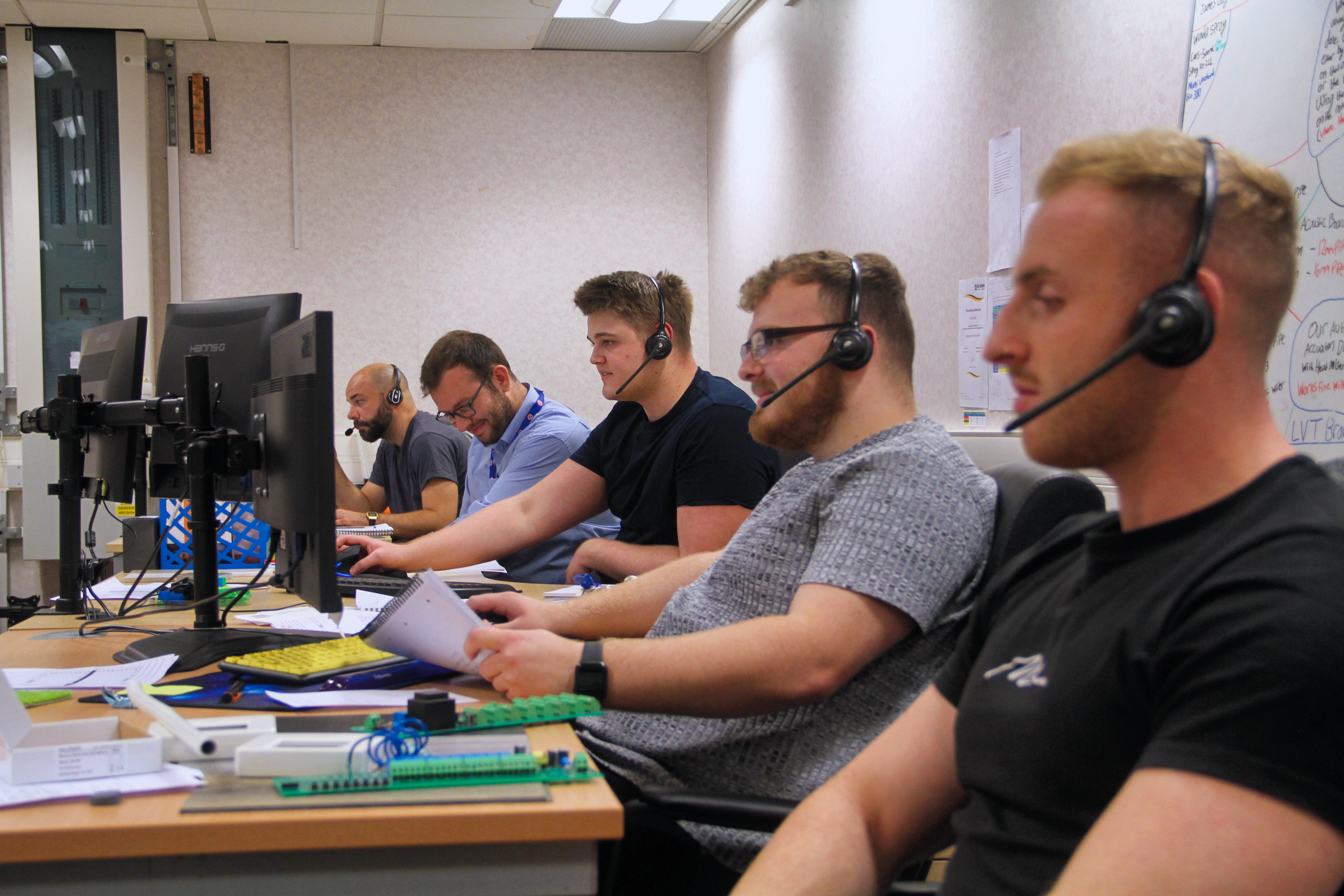 5 men sat at their desks with headsets on in front of their computers, the tech team