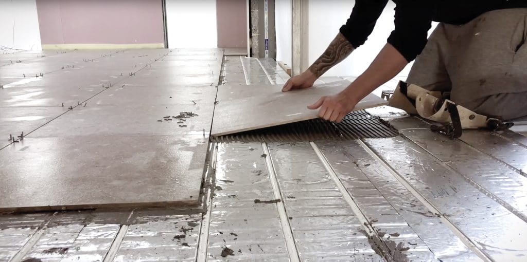 A tradesman laying new tiles over a Wunda underfloor heating system