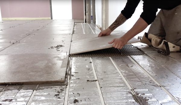 A tradesman laying new tiles over a Wunda underfloor heating system
