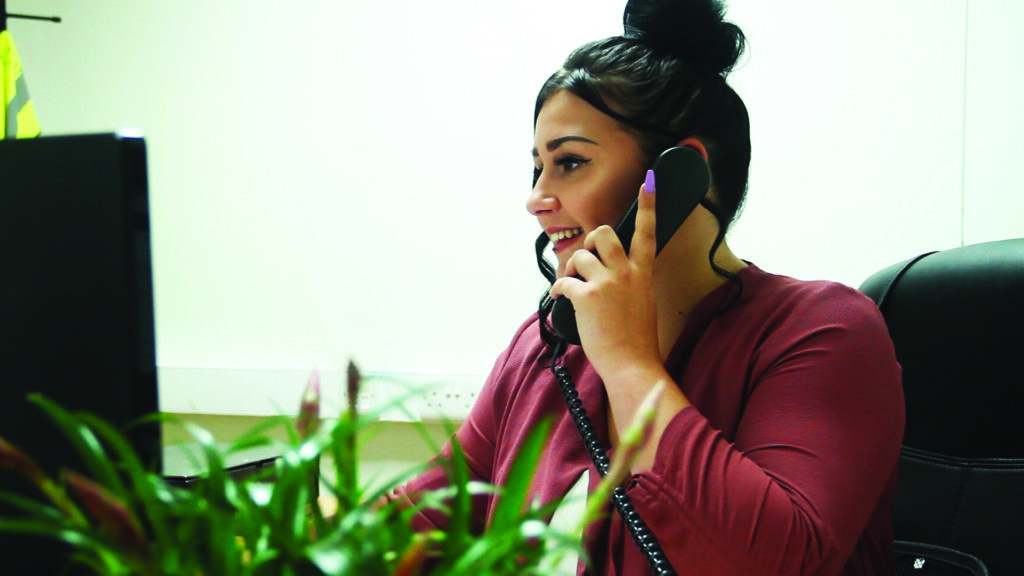 lady with a phone to her ear sat at desk in an office with plant in foreground