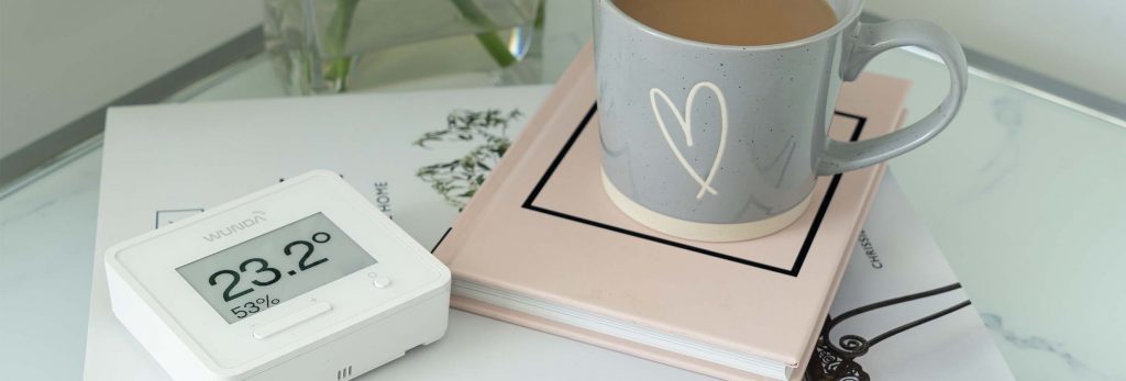 a WundaSmart Thermostat on a side table with a pink book and grey mug