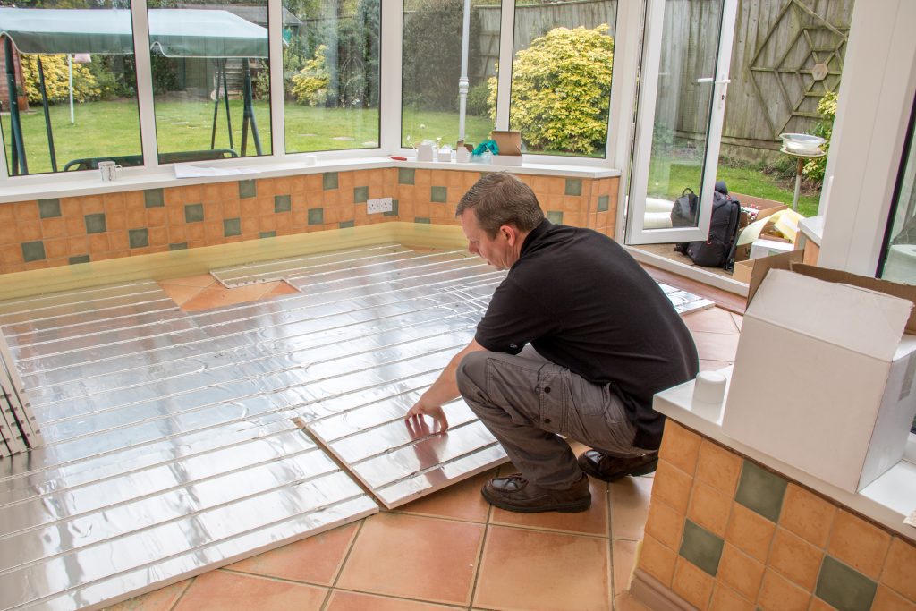 Tradesman installing underfloor heating boards inside a conservatory